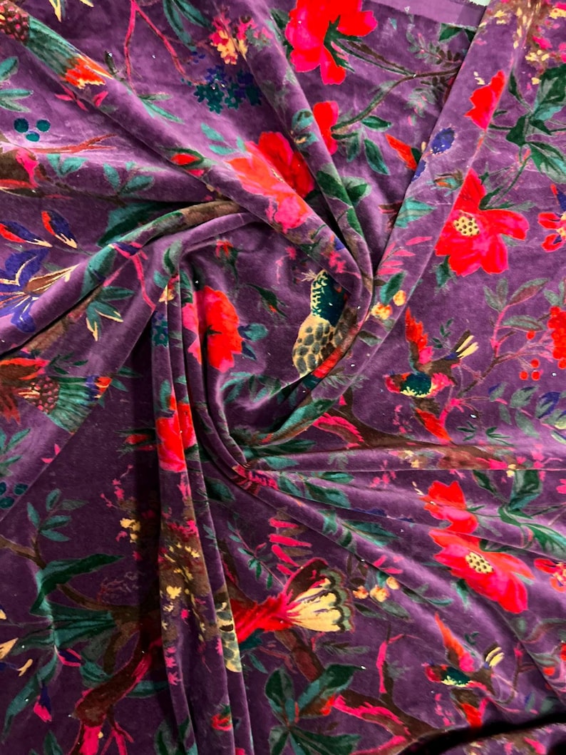 May include: A deep purple velvet fabric featuring a vibrant floral and bird pattern. The design includes bright red flowers, green leaves, and multi-colored birds perched on branches, creating a rich, textured surface with soft folds.