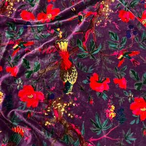 May include: A deep purple velvet fabric featuring a vibrant botanical print. The pattern displays bright red flowers, green leaves, and colorful birds perched on brown branches. The texture of the velvet creates subtle light and shadow effects.