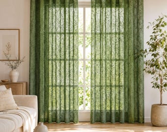 May include: A pair of floor-length, semi-sheer curtains in a deep olive green hue, featuring a delicate, repeating botanical vine pattern. The curtains are hung from a wooden rod using integrated metal grommets, creating uniform vertical folds.