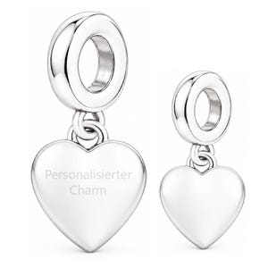 Pode incluir: Dois berloques prateados polidos em forma de coração com argolas circulares. O berloque maior apresenta o texto gravado "Personalisierter Charm" na superfície frontal, enquanto o berloque menor é liso e possui um acabamento brilhante.