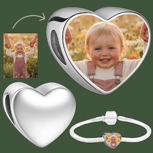 Könnte beinhalten: Ein herzförmiger Silber-Charm mit einem individuellen Foto eines Kleinkindes in rosa Kleidung. Der Charm wird leer, mit Fotoeinsatz und auf einem silbernen Schlangenketten-Armband dargestellt. Das Design hat eine glatte, polierte Oberfläche.