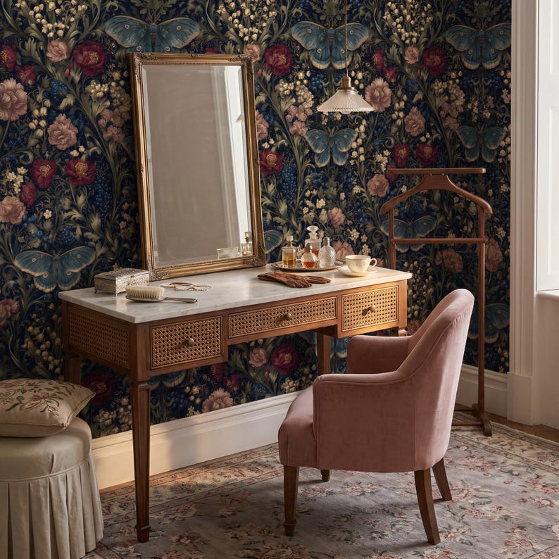 May include: A wooden vanity desk with a white marble top, three drawers featuring cane webbing, and a gold-framed mirror. A pink velvet armchair sits beside the desk, which holds a hairbrush, gloves, and glass bottles. A wooden valet stand is nearby.