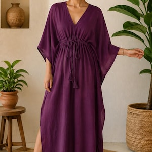 Può includere: Un abito caftano lungo fino ai piedi di colore viola intenso con scollo a V, maniche ampie a kimono e vita con coulisse e nappe. Il capo è realizzato in tessuto leggero e presenta spacchi laterali che partono dall'orlo inferiore.