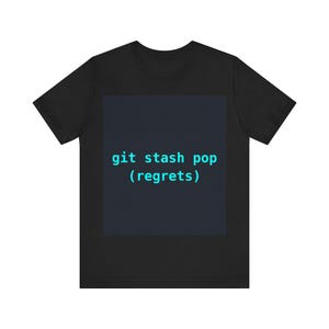 Op de afbeelding: Zwart T-shirt met de tekst "git stash pop (regrets)" in turquoise op een donkerblauwe vierkant. Het T-shirt heeft een ronde hals en korte mouwen. De tekst verwijst naar een softwareontwikkelingsopdracht.