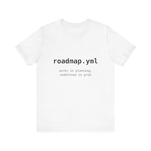 May include: A white short-sleeved t-shirt featuring black text that reads roadmap.yml followed by smaller grey text that reads works in planning, undefined in prod. The shirt has a crew neckline and a standard fit with a plain white back.