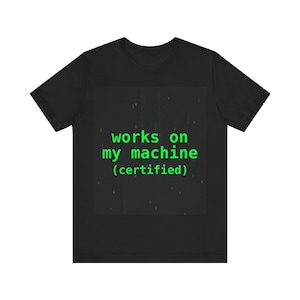 Może przedstawiać: Czarny t-shirt z zielonym napisem "works on my machine (certified)". Tekst jest wyśrodkowany na przodzie koszulki. Koszulka ma okrągły dekolt i krótkie rękawy.