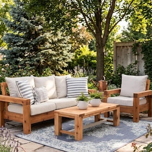 May include: A wooden outdoor furniture set consisting of a sofa and an armchair with beige cushions, striped throw pillows, and a rectangular wooden coffee table. Two small potted plants sit on the table, which rests on a blue patterned rug.