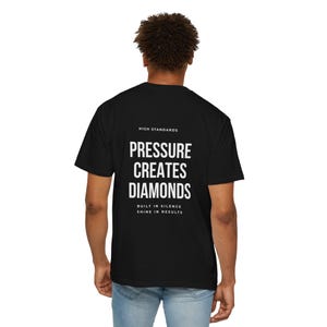 Könnte beinhalten: Schwarzes T-Shirt mit dem weißen Text "PRESSURE CREATES DIAMONDS" sowie den Sätzen "HIGH STANDARDS" und "BUILT IN SILENCE SHINE IN RESULTS". Das T-Shirt hat einen Rundhalsausschnitt.