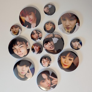 May include: A collection of circular, black and white badges displaying portraits of young people. The badges are of varying sizes and are arranged on a white surface. The images on the badges are of different people.