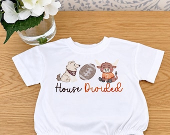 Könnte beinhalten: Ein weißer kurzärmeliger Baby-Body mit einer Stickerei, die einen Hund, einen Football und ein Stier-Maskottchen zeigt. Unter den Grafiken ist der Text House Divided in brauner und orangefarbener Schreibschrift eingestickt.