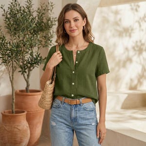 May include: An olive green short-sleeved button-down shirt with a round neckline, paired with light blue denim jeans featuring a tan leather belt and a woven straw handbag. The shirt has a vertical row of white buttons down the center front.