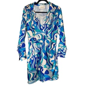 Puede incluir: Vestido cruzado de manga larga con un vibrante estampado abstracto en tonos azules, turquesas y blancos. El vestido presenta un cuello camisero y puños abotonados. La tela tiene un brillo sedoso.
