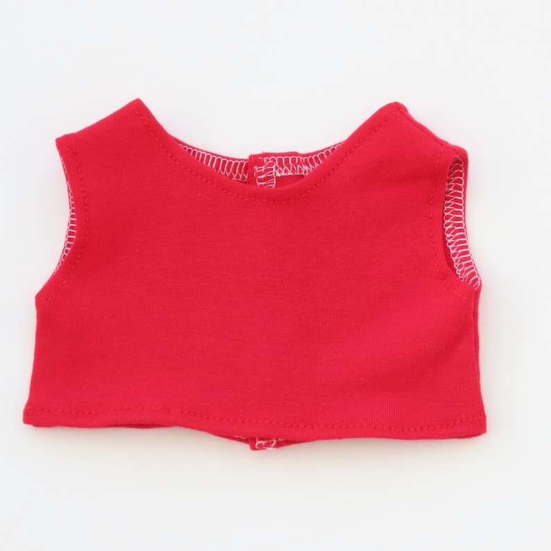 May include: A bright red doll-sized top with white stitching along the edges. The sleeveless top has a rounded neckline and a small button closure at the back. The fabric appears to be a soft knit material.