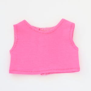 May include: A bright pink sleeveless top, likely for a doll or small figure. The top is made of a soft fabric and features a simple, rounded neckline and armholes. The edges are neatly stitched, and the overall design is minimalist.