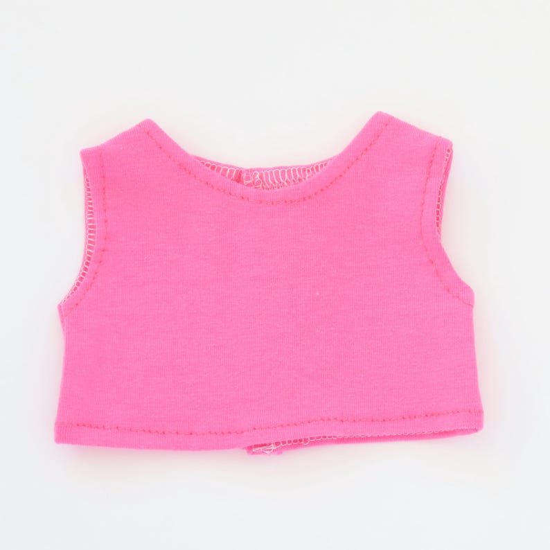 May include: A bright pink sleeveless top, likely for a doll or small figure. The top is made of a soft fabric and features a simple, rounded neckline and armholes. The edges are neatly stitched, and the overall design is minimalist.