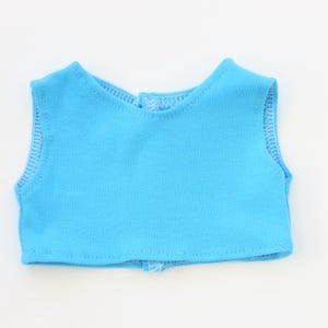 May include: A light blue doll vest with white stitching around the edges. The vest has a round neckline and a small opening in the back. The vest is made of a soft, lightweight fabric.