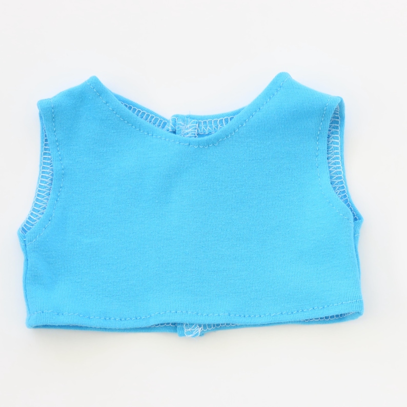May include: A light blue doll vest with white stitching around the edges. The vest has a round neckline and a small opening in the back. The vest is made of a soft, lightweight fabric.