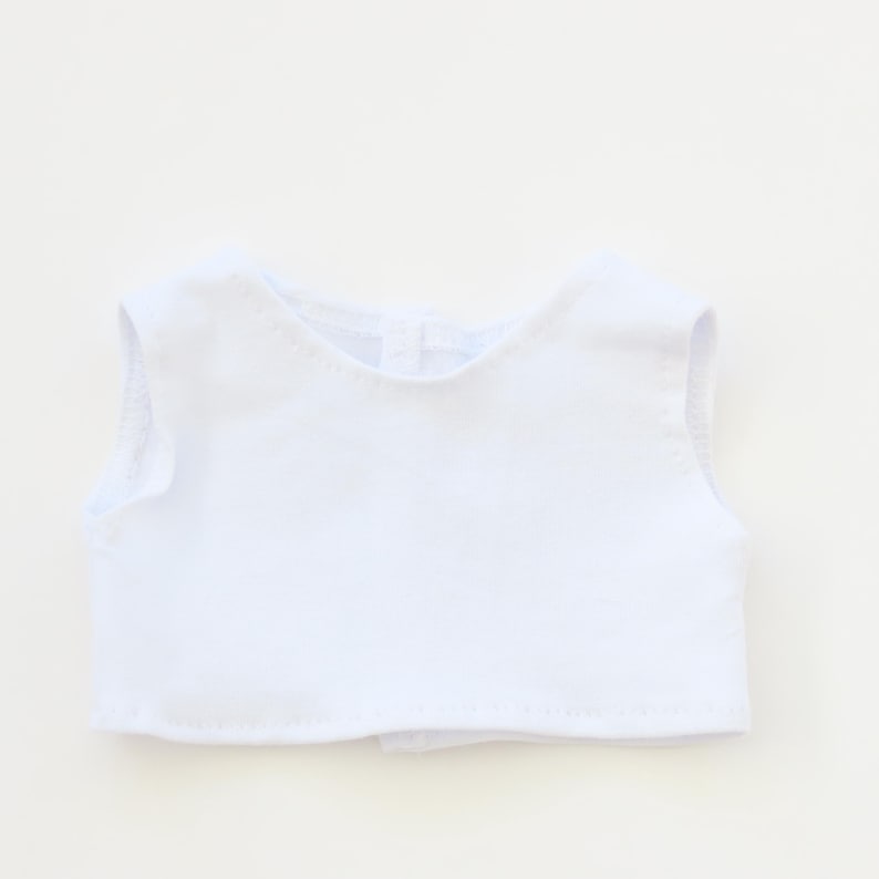 May include: A sleeveless white garment, possibly a top or vest, is centered against a white background. The garment has a rounded neckline and a button closure at the back. The fabric appears to be a soft, lightweight material.