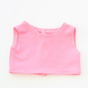 May include: A sleeveless, light pink top made of soft fabric. The top has a rounded neckline and a small opening at the back. The edges are finished with a delicate white stitch.