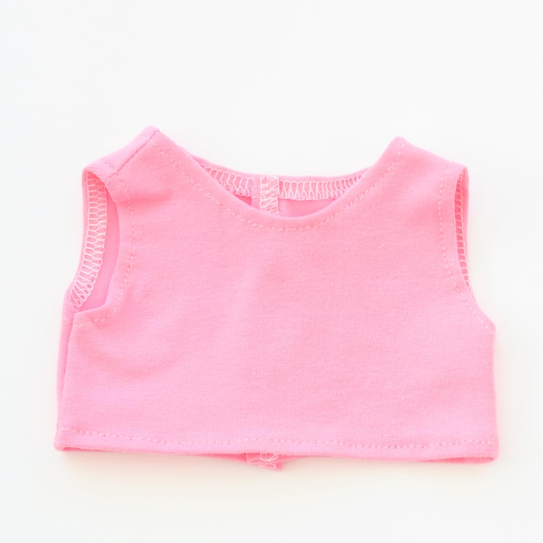 May include: A sleeveless, light pink top made of soft fabric. The top has a rounded neckline and a small opening at the back. The edges are finished with a delicate white stitch.