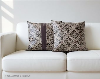 May include: Two decorative throw pillows with a damask pattern in shades of brown and gray, resting on a white leather sofa. One pillow features a vertical brown stripe. The pillows add a touch of elegance to the living room.