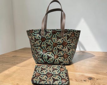 May include: A patterned tote bag and matching wallet. The bag has a brown and teal floral design with brown handles. The wallet has the same pattern. The items are on a wooden surface.