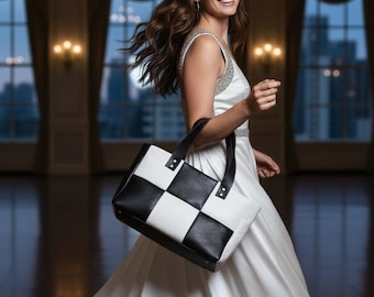 May include: A rectangular tote bag featuring a bold black and white checkered pattern. The bag is constructed with smooth, solid-colored black and white panels arranged in a grid, complemented by two sturdy black leather-like handles attached with rivets.