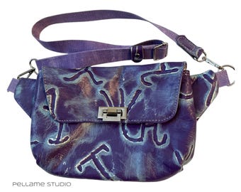 May include: A purple leather crossbody bag with a flap closure and a silver-colored clasp. The bag features a unique pattern in shades of blue and white. It has an adjustable strap and a small, matching strap detail. The bag is designed with a modern aesthetic.