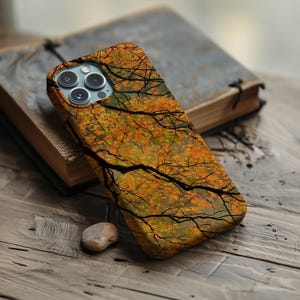 May include: A smartphone case featuring a detailed print of autumn tree branches with orange, yellow, and green leaves against a dark background. The case has a cutout for a triple-lens camera system on the upper left corner.