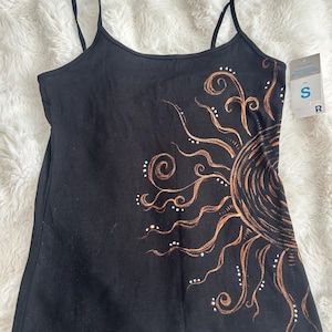 May include: Black vest top with thin straps, featuring a copper-coloured sun design. The sun design has swirling lines and white dot accents. A small tag is attached to the top.
