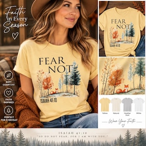 May include: A pale yellow t-shirt featuring a graphic of a forest with a small fox, the text FEAR NOT, and the scripture reference ISAIAH 41:10. The design includes watercolor-style trees in shades of orange, green, and blue on a light background.