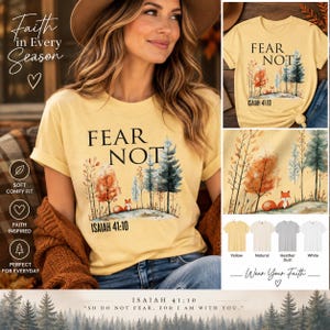 May include: A pale yellow t-shirt featuring a graphic of a forest with a small fox, the text FEAR NOT, and the scripture reference ISAIAH 41:10. The design includes watercolor-style trees in shades of orange, green, and blue on a light background.