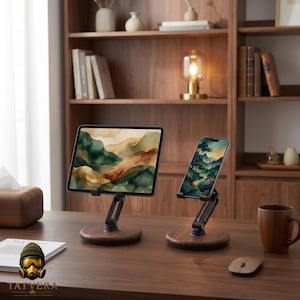 Op de afbeelding: Twee verstelbare apparaathouders met ronde donkerhouten voetstukken en zwarte metalen armen. De ene houder bevat een tablet met een aquarel landschap, de andere een smartphone met een soortgelijke natuurafbeelding. De houders staan op een bureau.