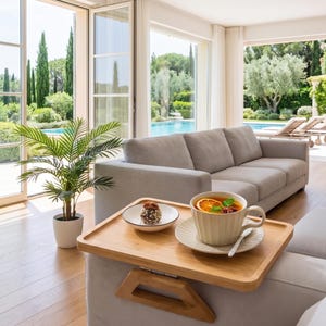 May include: A rectangular bamboo sofa arm tray table with a light wood finish, featuring a cup of tea with orange slices and a small bowl with a chocolate treat. The tray is placed over the arm of a light gray sofa in a bright living room.