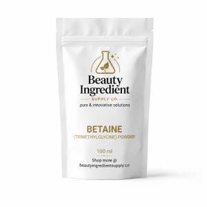 Peut inclure: Un sachet blanc debout contenant de la poudre de bétaïne (triméthylglycine). L'étiquette présente une icône de fiole dorée avec une feuille, le texte Beauty Ingredient Supply Co., pure & innovative solutions, 100 ml et beautyingredientsupply.co.