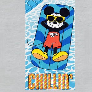 May include: A beach towel featuring Mickey Mouse relaxing on a blue and white striped pool float, wearing yellow sunglasses and red shorts. The towel has the word "CHILLIN'" in orange and yellow block letters.