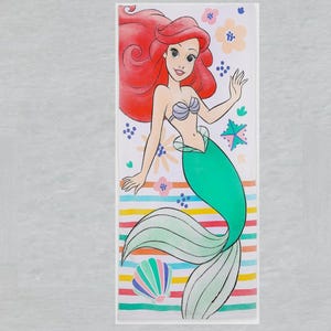 May include: A rectangular illustration of a mermaid with red hair, a teal tail, and a seashell top. The background features flowers, stars, and a striped pattern in various colors. A seashell is also included in the design.