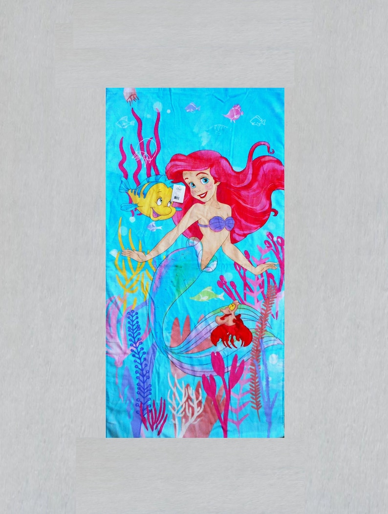 May include: A rectangular beach towel featuring a vibrant illustration of Ariel, the Little Mermaid, with her red hair and purple seashell top. The design includes Flounder, Sebastian, and colorful underwater plants against a blue background.