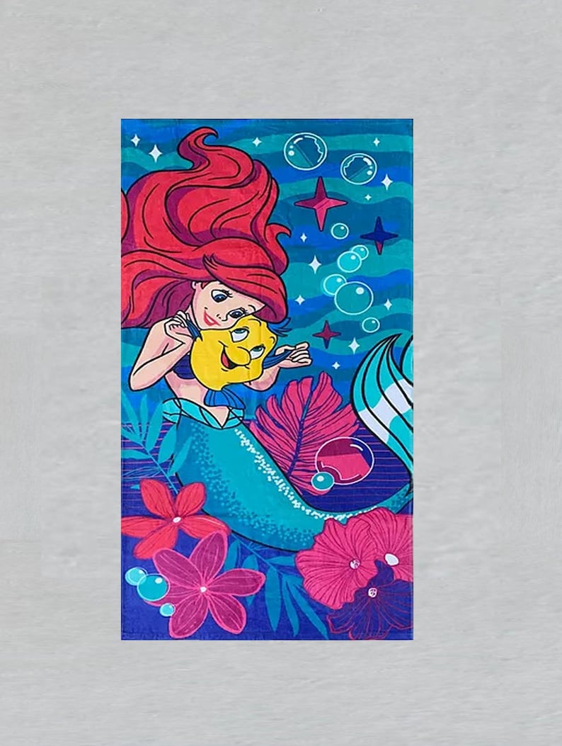 Puede incluir: Una toalla de playa rectangular con una colorida ilustraci&oacute;n de Ariel de La Sirenita. Ariel tiene el pelo rojo y una cola azul, sosteniendo un pez amarillo. El fondo incluye burbujas, estrellas y flores rosas y rojas.