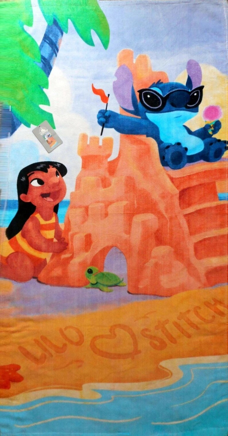 May include: Beach towel featuring a colorful illustration of Lilo and Stitch at the beach. Stitch wears sunglasses and holds a flag and ice cream. Lilo is next to a sandcastle. The words "Lilo" and "Stitch" are written in the sand.