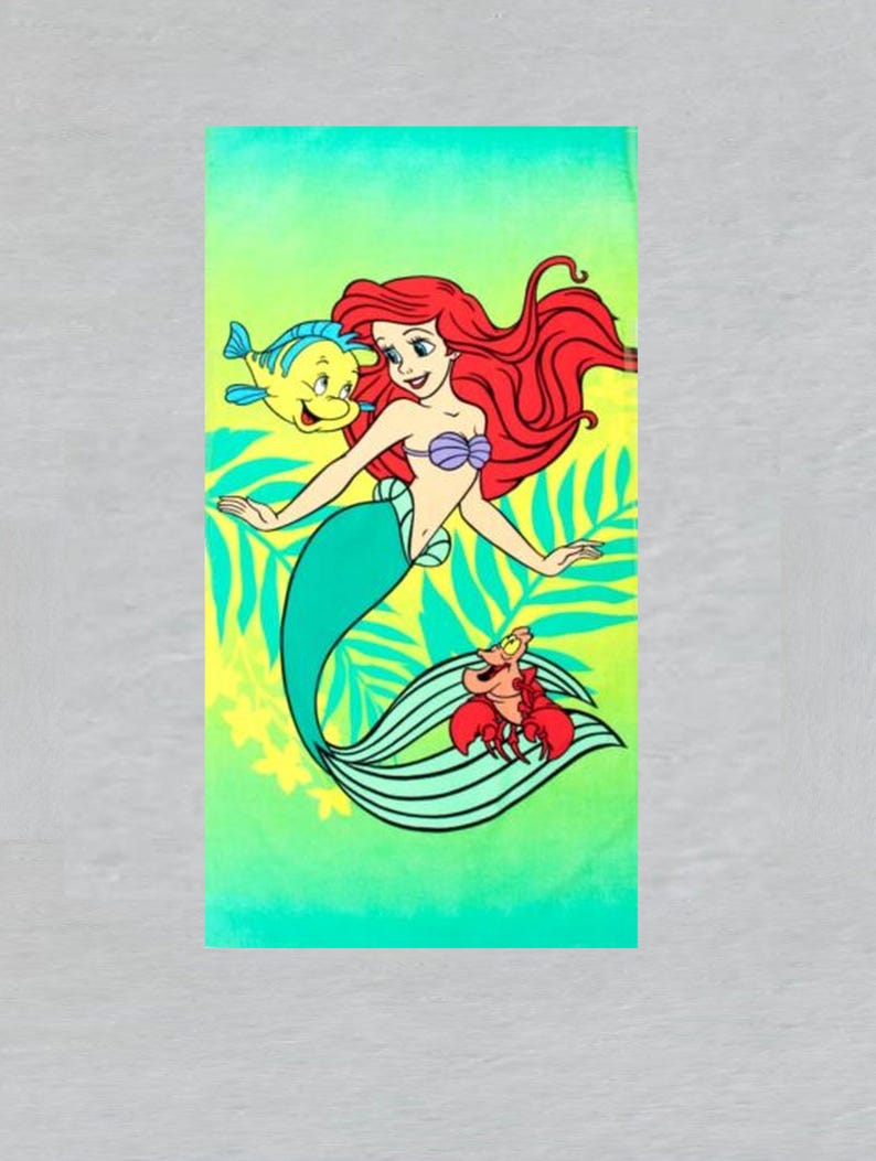 May include: A rectangular beach towel featuring a cartoon illustration of a mermaid with red hair, a teal tail, and a purple seashell top. A yellow fish and a red crab are also depicted. The background is a gradient of green and yellow.