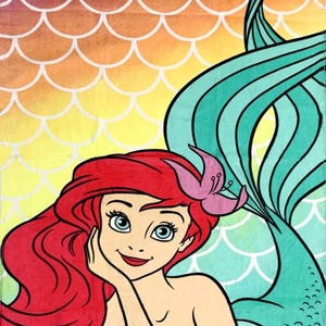 May include: A colorful beach towel featuring a cartoon mermaid with red hair, a pink flower, and a teal tail. The background has a gradient of purple, orange, and yellow with a white scale pattern.