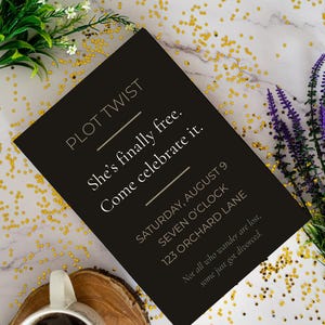 May include: A black rectangular invitation card with gold text reading PLOT TWIST, She’s finally free. Come celebrate it. SATURDAY, AUGUST 9, SEVEN O’CLOCK, 123 ORCHARD LANE, and Not all who wander are lost, some just got divorced.