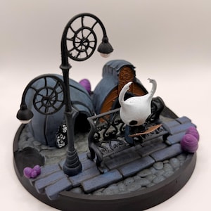 May include: A 3D printed diorama featuring a white, horned character sitting on a black ornate bench. The scene includes two blue-grey domed structures, a tall black spiral-topped lamppost, and small purple egg-shaped objects on a stone base.