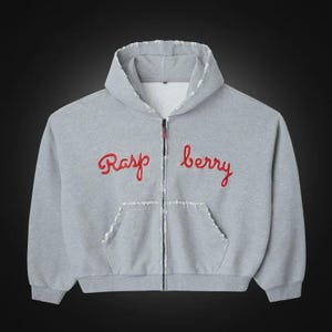May include: A light gray zip-up hoodie featuring a white mesh-lined hood and distressed, frayed edges along the hood, front pocket, and zipper line. The word Raspberry is embroidered in red cursive script across the chest in two separate parts.