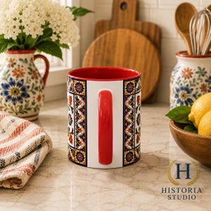 May include: A ceramic mug featuring a vibrant, multi-colored floral pattern in shades of blue, orange, and yellow, with a solid red handle and a matching red interior. The exterior design is arranged in vertical panels separated by white borders.