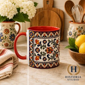 May include: A ceramic mug featuring a vibrant, multi-colored floral pattern in shades of orange, blue, and green against a white background. The mug has a solid red handle and a matching red interior, with a decorative border design.
