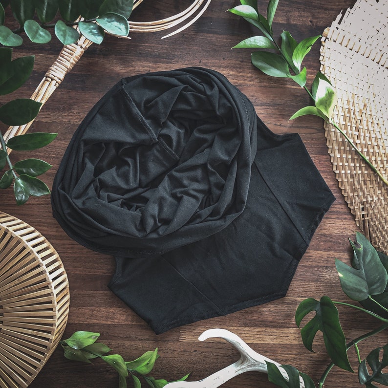 May include: A black hooded cowl neck top made of a soft, stretchy fabric. The cowl neck is gathered and draped, creating a loose and comfortable fit.