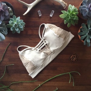 May include: A white lace bralette with adjustable straps and a criss-cross design in the front. The bralette is made of a soft, stretchy fabric and has a delicate lace trim.