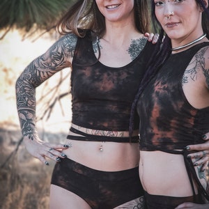 May include: Two women wearing black and brown tie-dye crop tops and matching shorts. Both women have tattoos and piercings.